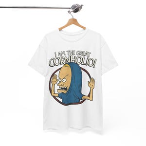 May include: White t-shirt featuring a cartoon character with a blue hood and the phrase "I AM THE GREAT CORNHOLIO!" in black and red lettering. The character is inside a brown and black circle, with arms raised.