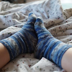 Pode incluir: Close-up de dois p&eacute;s usando meias listradas azuis e brancas. As meias est&atilde;o em uma cama com uma colcha estampada floral. As meias t&ecirc;m uma apar&ecirc;ncia texturizada.