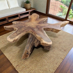 Può includere: Un tavolino da caffè in legno fatto a mano con una forma naturale e organica. Il tavolo presenta un design a stella con un colore marrone chiaro e venature del legno visibili. Poggia su una base scultorea robusta e su un tappeto tessuto.
