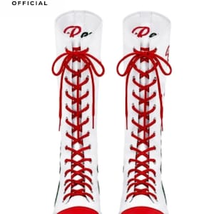 May include: A pair of white mid-calf boots featuring bright red rounded toe caps and matching red laces that crisscross up the front. The top of the boots displays red cursive text, and the upper left corner includes a black triangular logo with the text LUXURY SHOSE OFFICIAL.