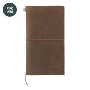 May include: A brown leather journal with a matching elastic closure. The journal has a rectangular shape and a small embossed logo on the bottom right corner. A green circle with Japanese text is in the top left corner.