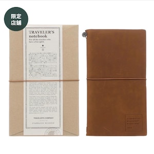 May include: A brown leather Traveler's notebook with a matching brown elastic closure, next to a brown paper package. The notebook has the text "TRAVELER'S notebook" and "STARBUCKS RESERVE ROASTERY" printed on it.