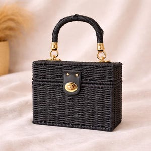 May include: A black woven handbag with a rectangular shape. It features a curved handle and gold-colored hardware. The bag has a clasp closure with a gold-colored lock. The bag is approximately 6 inches wide, 5 inches tall, and 4 inches deep.