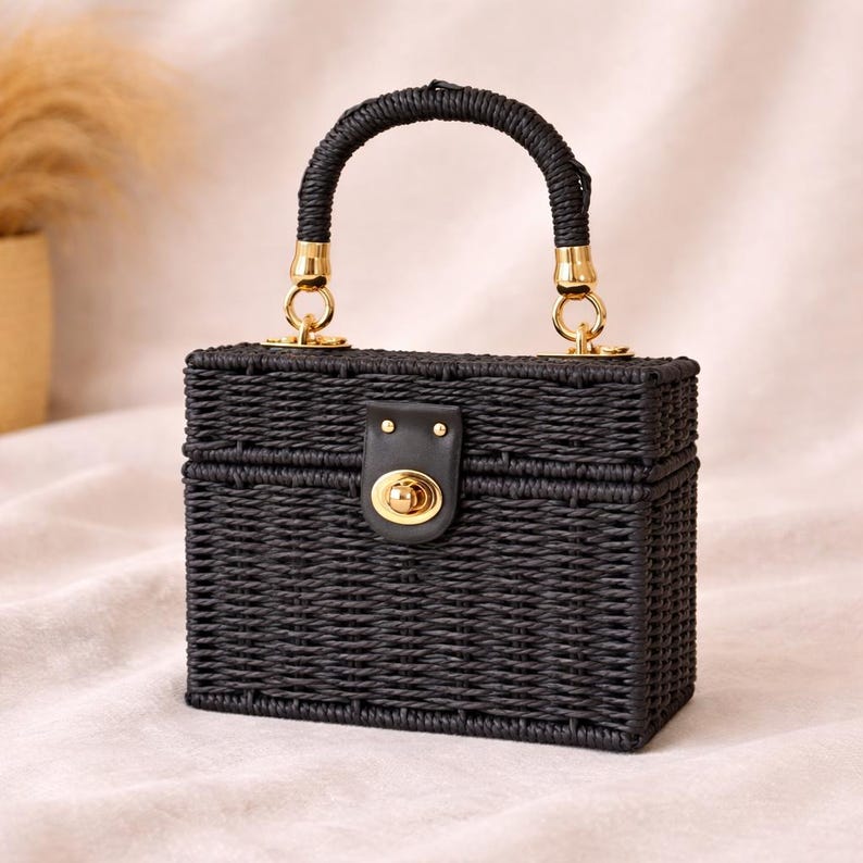 May include: A black woven handbag with a rectangular shape. It features a curved handle and gold-colored hardware. The bag has a clasp closure with a gold-colored lock. The bag is approximately 6 inches wide, 5 inches tall, and 4 inches deep.