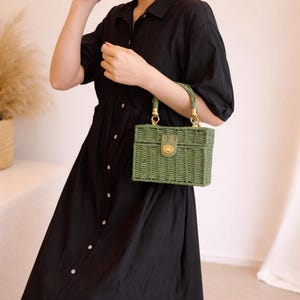May include: A green woven handbag with a rectangular shape and a top handle. The bag features a gold-colored clasp and hardware. The handle is also green and appears to be made of a woven material.