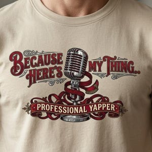 Puede incluir: Camiseta beige con un diseño vintage. Presenta un micrófono plateado con una cinta roja y el texto "Because Here's My Thing.." encima. Debajo, se lee "Professional Yapper".