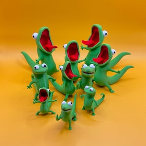 May include: A collection of green lizard figurines with open mouths and red tongues. The lizards have white eyes and are posed in various positions. The background is a solid yellow color.