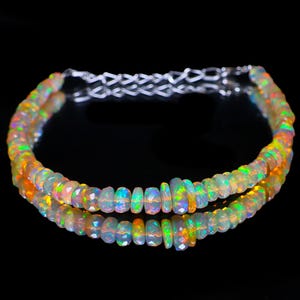 May include: A faceted opal bead bracelet with a silver chain clasp. The beads display a range of colours, including orange, green, and blue, with a reflective surface. The bracelet is displayed on a reflective black surface.