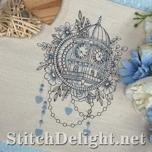 Può includere: Ricamo di un orologio con tetto a cupola, circondato da fiori e foglie. Il disegno è in tonalità blu e nero su tessuto color crema. Il testo "StitchDelight.net" è in basso.