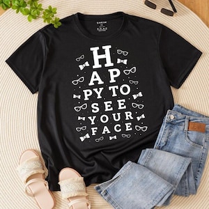 May include: Black t-shirt with the text "HAPPY TO SEE YOUR FACE" in white, surrounded by eyeglasses and bow ties. The shirt is paired with blue jeans and sandals.