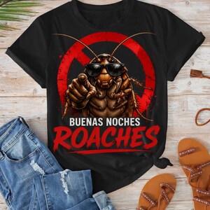 May include: Black t-shirt featuring a cartoon cockroach wearing sunglasses and pointing. The design includes a red circle with a line through it and the words "BUENAS NOCHES ROACHES" in red. The shirt is paired with blue jeans and brown sandals.