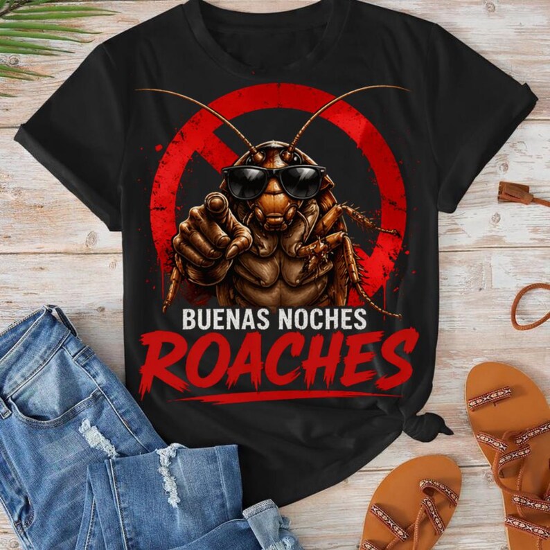 May include: Black t-shirt featuring a cartoon cockroach wearing sunglasses and pointing. The design includes a red circle with a line through it and the words "BUENAS NOCHES ROACHES" in red. The shirt is paired with blue jeans and brown sandals.