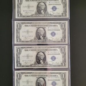 Pode incluir: Quatro certificados de prata de um dólar vintage. Cada nota apresenta um retrato de George Washington e o texto "Silver Certificate" e "One Dollar". As notas estão em capas protetoras.