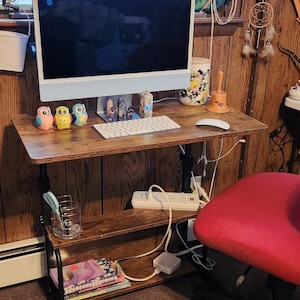 May include: A brown adjustable-height desk with a computer monitor, keyboard, and mouse. Decorative owl figurines sit on the desk. A red office chair is next to the desk. A window and decorative items are in the background.