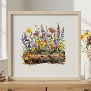 May include: Cross-stitch artwork of a vibrant flower garden in a wooden planter. The artwork features yellow, purple, and pink flowers, with green foliage. The framed piece is displayed on a wooden surface.