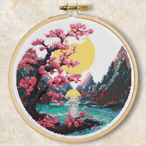 May include: Cross-stitch embroidery depicting a tranquil landscape with a cherry blossom tree, pink flowers, a yellow sun, and mountains. The scene is set over a turquoise lake, within a wooden embroidery hoop.