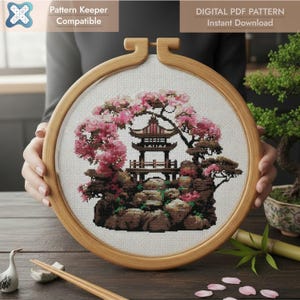 Könnte beinhalten: Eine Kreuzstichstickerei in einem Holzrahmen zeigt eine japanische Pagoden-Szene mit rosa Kirschblüten. Das Design umfasst eine detaillierte Pagode, Felsen und Bäume. Der Text "Pattern Keeper Compatible" und "DIGITAL PDF PATTERN Instant Download" sind sichtbar.