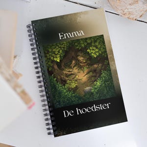 Può includere: Quaderno a spirale con illustrazione di una foresta. La copertina presenta il nome "Emma" e il titolo "De hoedster". L'illustrazione mostra una scena di foresta verde con alberi e vegetazione.