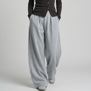 Può includere: Una persona indossa un cardigan marrone scuro con bottoni e pantaloni della tuta grigio chiaro. Il cardigan ha maniche lunghe e una trama a coste. I pantaloni della tuta sono a gamba larga e dalla vestibilità ampia. L'outfit è semplice e casual.