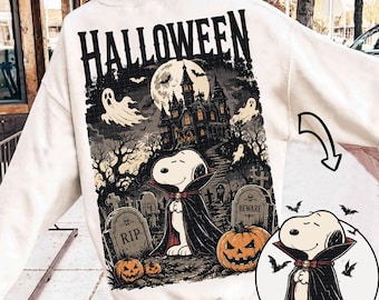 May include: A white long-sleeve sweatshirt featuring a large graphic on the back with the text HALLOWEEN. The design depicts a cartoon dog dressed as a vampire in a graveyard with a haunted house, ghosts, bats, a full moon, and pumpkins.