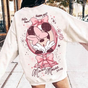 May include: Cream-coloured sweatshirt with a Minnie Mouse graphic in a pink mirror frame. The design includes bows, stars, and the text "Hello, there!" and "Happy girl!" along with "Minnie Mouse xoxo".