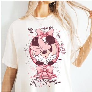 May include: Off-white t-shirt with a pink Minnie Mouse design. The graphic shows Minnie Mouse in a mirror, bows, and the text "Hello, there! Happy girl! Minnie Mouse xoxo." The design also includes the text "Why settle for less fun?"