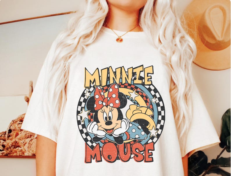 Puede incluir: Camiseta color crema con un dise&ntilde;o retro de Minnie Mouse. El dise&ntilde;o incluye la cara de Minnie, un lazo de lunares y las palabras "MINNIE MOUSE" en una fuente vintage. El gr&aacute;fico est&aacute; sobre un fondo a cuadros y lleno de estrellas.