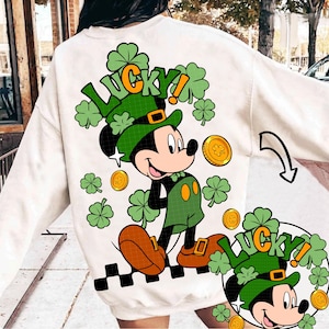 May include: Cream-colored sweatshirt featuring a cartoon Mickey Mouse dressed as a leprechaun, with a green hat and overalls. The word "LUCKY!" is printed above the character in green and orange, surrounded by shamrocks and gold coins.