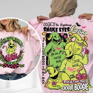 May include: Pink sweatshirt featuring a graphic of Oogie Boogie from The Nightmare Before Christmas. The front has a circular design with the text "Well, Well, Well, What Have We Here?". The back displays Oogie Boogie and the text "Snake Eyes Casino".