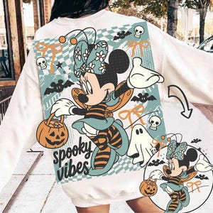 May include: A white sweatshirt featuring a large graphic print of a cartoon mouse dressed as a bee, holding a jack-o'-lantern bucket. The design includes a teal checkered background, skulls, bats, ghosts, bows, and the text spooky vibes in black.