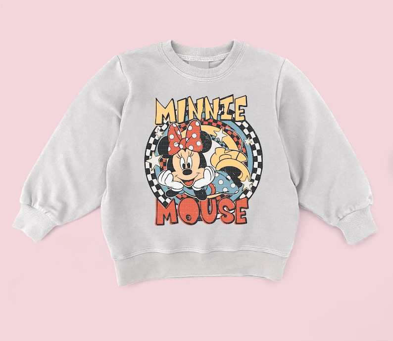 Puede incluir: Sudadera gris claro con un dise&ntilde;o de Minnie Mouse. El dise&ntilde;o incluye la cara de Minnie, un lazo rojo con lunares blancos y las palabras "MINNIE MOUSE" en una fuente retro. El dise&ntilde;o est&aacute; sobre un fondo a cuadros.