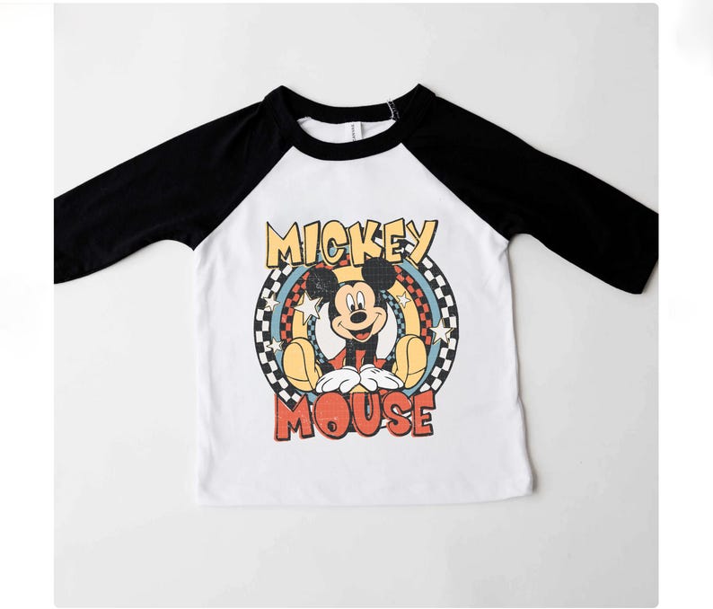 May include: A white and black raglan-style shirt with a Mickey Mouse graphic. The graphic features the words "Mickey Mouse" in a retro font. The shirt has black sleeves and a white body.