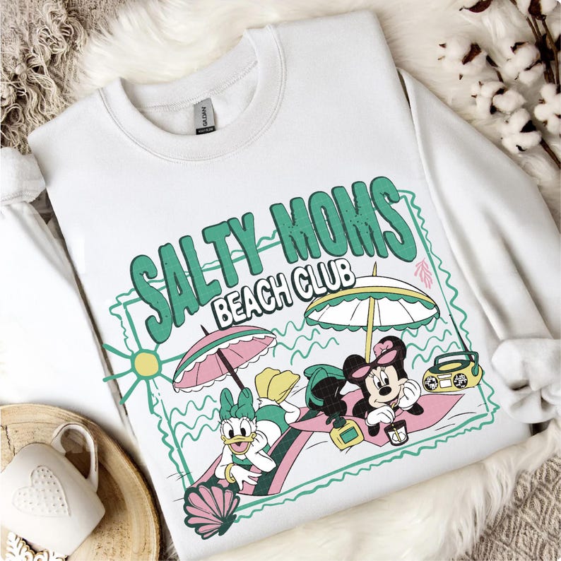 May include: White sweatshirt with a graphic that reads "SALTY MOMS BEACH CLUB" in green and pink. The graphic features cartoon characters under beach umbrellas, with a boombox and seashell.