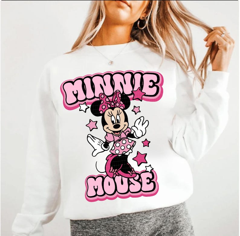 Peut inclure: Sweat-shirt blanc avec un motif de Minnie Mouse rose et noir. Le texte "MINNIE MOUSE" est en police bulle. Des &eacute;toiles roses entourent le dessin de Minnie Mouse.