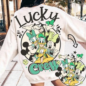 Könnte beinhalten: Cremefarbenes Sweatshirt mit einem kreisförmigen Grafikdesign von Disney-Figuren, darunter Mickey, Minnie, Donald, Daisy, Goofy und Pluto. Das Wort "Lucky" ist oben in einem Bogen angeordnet, darunter "Crew". Das Design enthält grüne und schwarze Akzente.