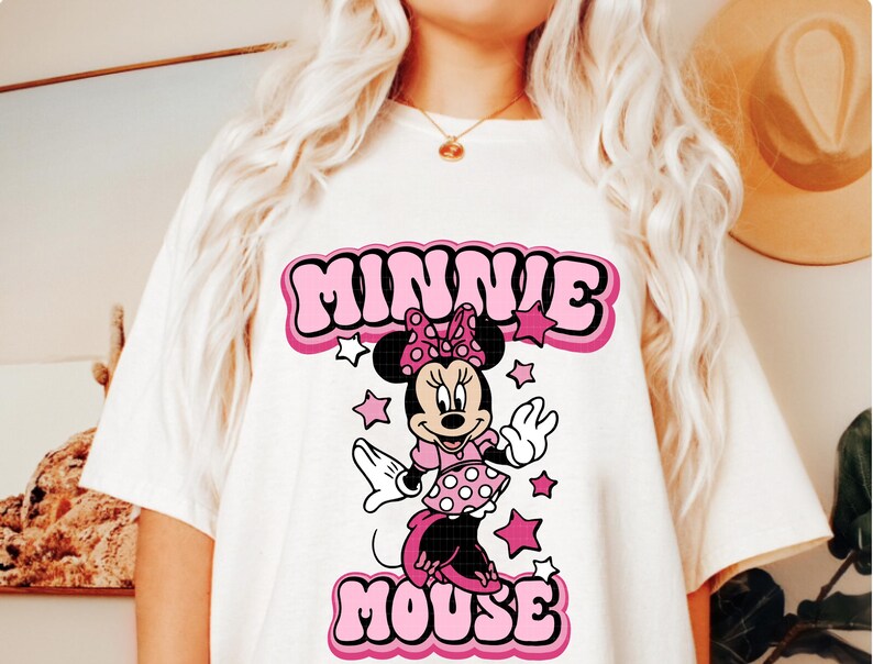 Peut inclure: T-shirt blanc avec un motif r&eacute;tro de Minnie Mouse. Le graphisme comprend les mots "MINNIE MOUSE" en lettres roses &agrave; bulles, avec Minnie Mouse au centre, entour&eacute;e d'&eacute;toiles roses. Le design a une esth&eacute;tique vintage et cartoon.