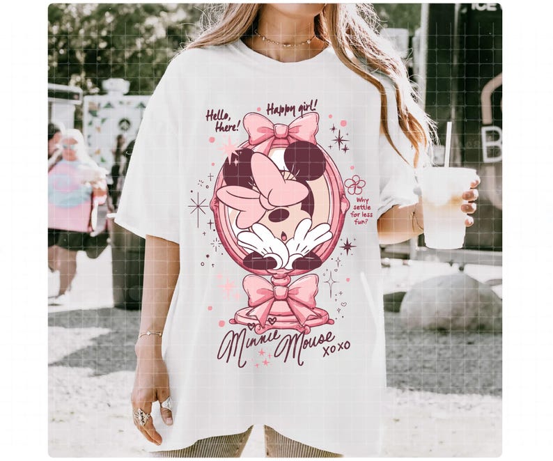 May include: White t-shirt with a Minnie Mouse graphic in a pink mirror frame and bows. The design includes the text "Hello, there! Happy girl! Minnie Mouse xoxo" and "Why settle for less fun!" A playful, whimsical design.