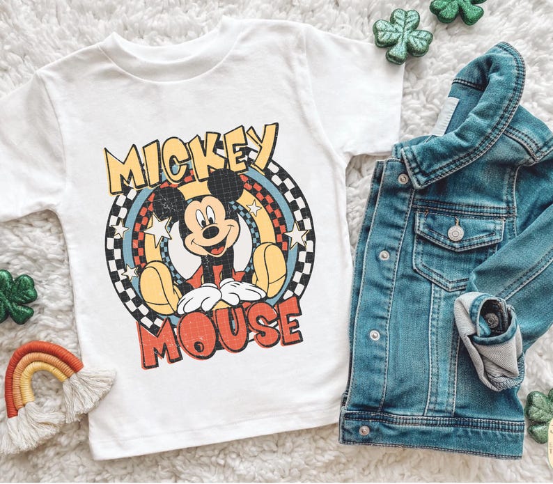 May include: White t-shirt with a Mickey Mouse graphic and the words "Mickey Mouse". A denim jacket is folded nearby. Small rainbow and shamrock decorations are also visible.