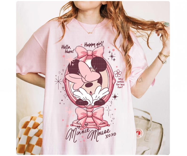 May include: A pale pink t-shirt with a Minnie Mouse design. The graphic shows Minnie in a mirror, bows, and the text "Hello, there! Happy girl! Minnie Mouse xoxo." Additional text reads "Why settle for less fun?"