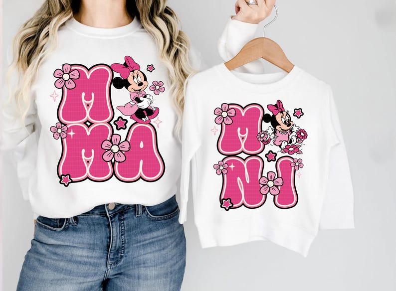 May include: White sweatshirts with pink text and Minnie Mouse graphics. One sweatshirt says "MAMA" and the other says "MINI". The text is in a bubble font with a black outline, and the Minnie Mouse graphic is in pink and black.