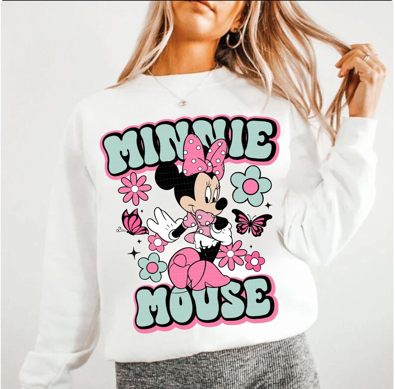 May include: White sweatshirt featuring a retro design of Minnie Mouse. The design includes the words "MINNIE MOUSE" in a teal and black font, along with pink flowers, butterflies, and Minnie Mouse in a pink polka dot dress.