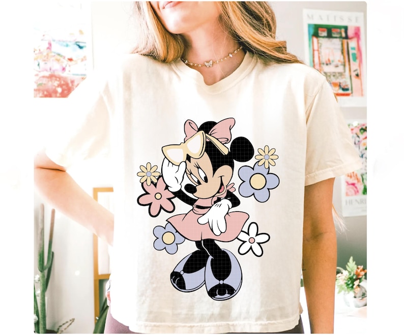 May include: Cream-colored t-shirt featuring a Minnie Mouse graphic. Minnie is depicted in a pink dress, bow, and sunglasses, surrounded by pastel flowers. The design is a playful and colorful illustration.