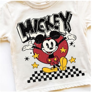 Puede incluir: Camiseta color crema con un dise&ntilde;o de Mickey Mouse de estilo vintage. El dise&ntilde;o incluye la palabra "MICKEY" en letras negras, Mickey Mouse en un c&iacute;rculo rojo, estrellas amarillas y un patr&oacute;n de cuadros blanco y negro.