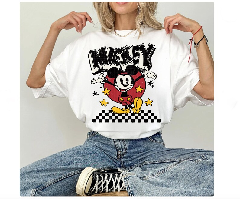 Puede incluir: Camiseta blanca con un gr&aacute;fico de Mickey Mouse y la palabra "Mickey" en negro. Mickey est&aacute; en un c&iacute;rculo rojo con estrellas amarillas y un borde a cuadros blanco y negro.