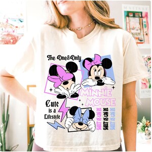 May include: Cream-colored t-shirt featuring a Minnie Mouse graphic. The design includes three images of Minnie Mouse with different colored bows, the text "The One & Only", "Cute is a Lifestyle", and "Sweet as can be".