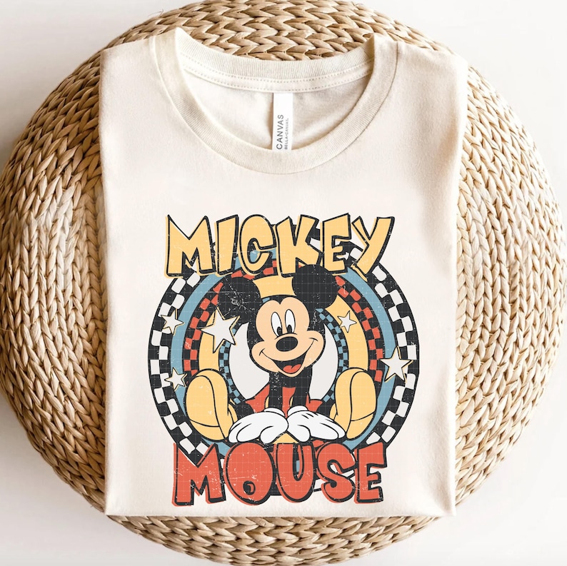 May include: Cream-coloured t-shirt featuring a retro design of Mickey Mouse. The graphic includes the words "MICKEY MOUSE" in a vintage font, with Mickey sitting inside a circular design with stars and a checkered pattern.