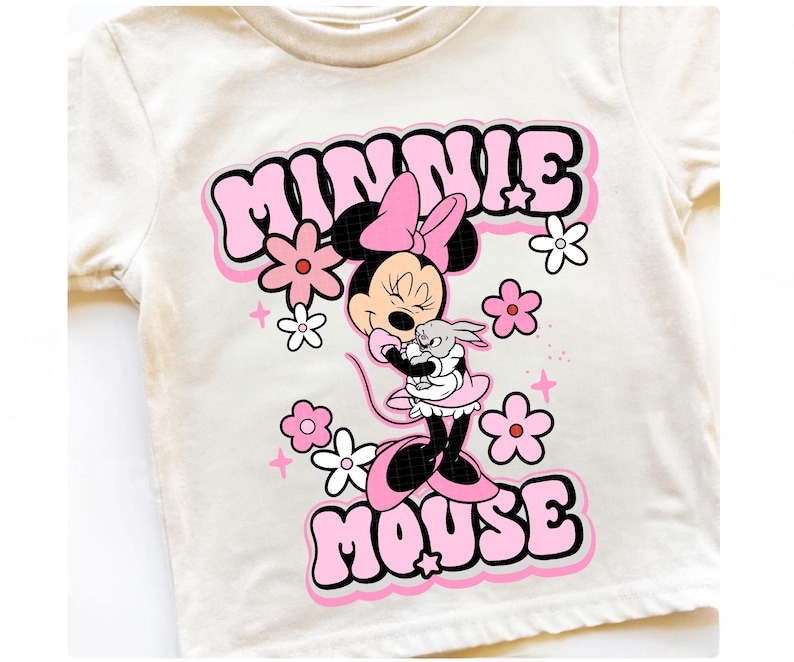 May include: Cream-colored t-shirt featuring a graphic of Minnie Mouse in a pink dress and bow, hugging a small gray bunny. The words "MINNIE MOUSE" are in pink bubble letters, surrounded by pink and white flowers.