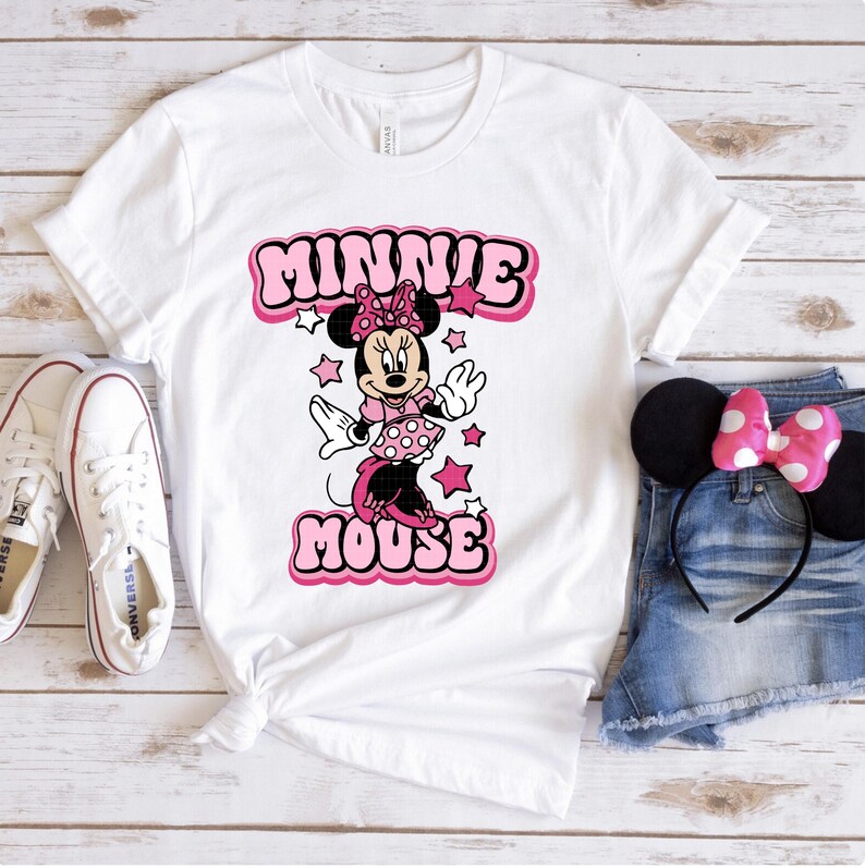 Peut inclure: T-shirt blanc avec un motif de Minnie Mouse rose et le texte "MINNIE MOUSE". L'image comprend des baskets blanches, un short en jean et des oreilles de Minnie avec un n&oelig;ud rose.