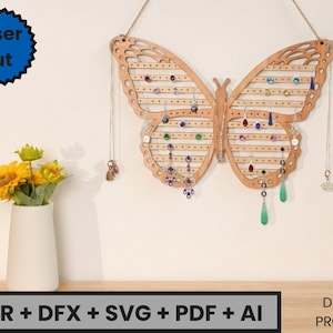 Op de afbeelding: Een houten vlinder-vormige sieraden organizer, laser gesneden, met gaten voor oorbellen en kettingen. De organizer hangt aan een touw. De afbeelding toont ook een witte vaas met gele bloemen en de tekst "CDR + DFX + SVG + PDF + AI".