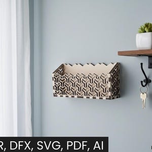 May include: A laser-cut wooden wall organizer with a geometric pattern. The organizer is mounted on a light blue wall, with a shelf and hooks visible. The text "CDR, DFX, SVG, PDF, AI" is at the bottom.